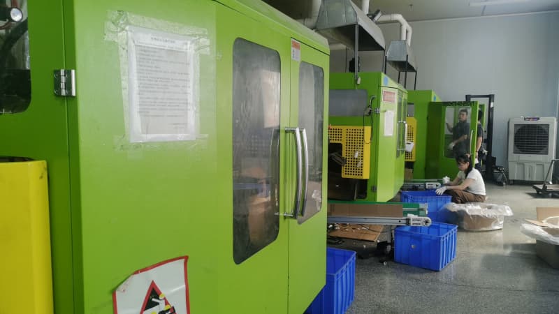 Multiple blow molding machines are arranged in the workshop, and a worker is sorting products beside the conveyor line