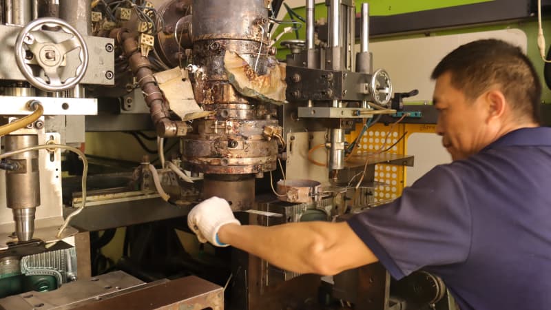 Worker wearing gloves adjusting the mold head of the blow molding machine, equipment with production usage traces