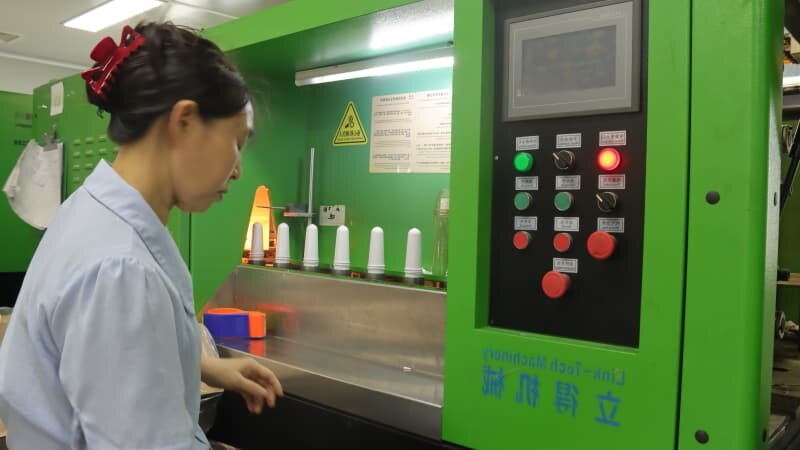 Worker operating Link-Tech blow molding machine, heated PET preforms arranged on the processing station