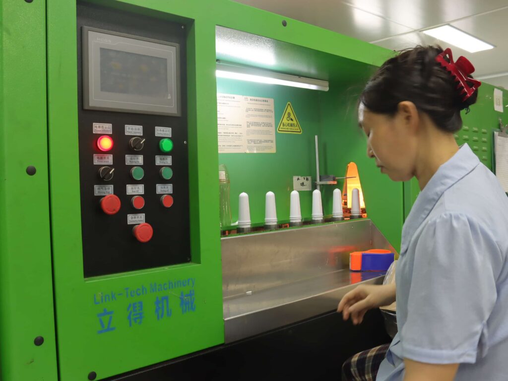 Factory worker inspecting white cosmetic plastic bottle preforms on blow molding machine