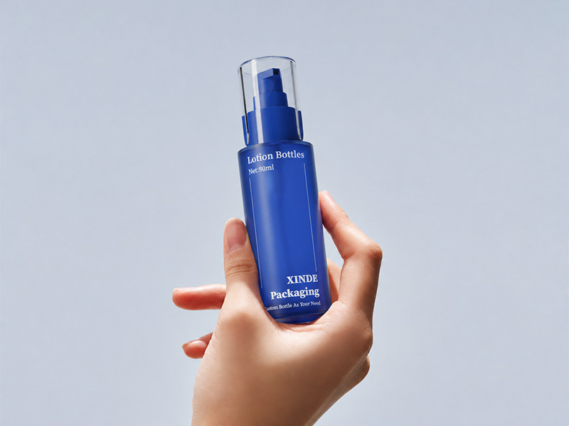 Matte blue 80ml plastic lotion bottle held in hand, empty portable cosmetic skincare packaging